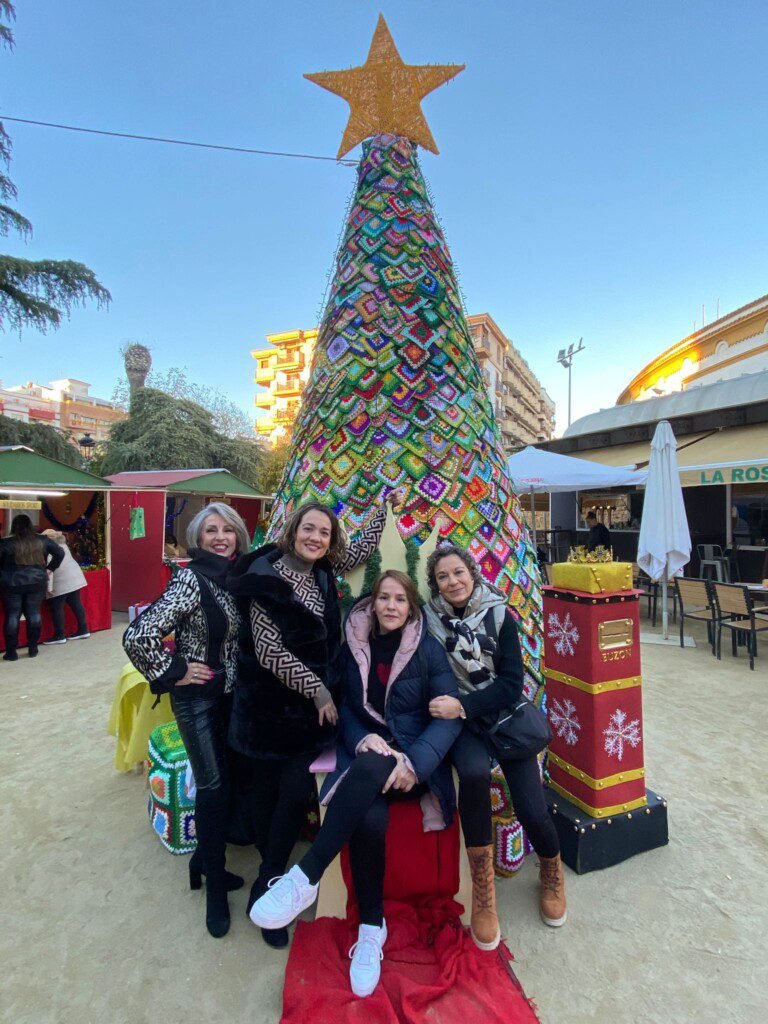 Miembros de la asociación junto a un gran árbol de Navidad decorado en el mercadillo solidario.